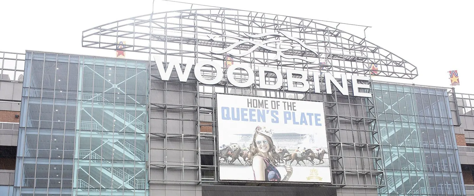 The glass and steel entrance facade of Woodbine Racetrack with a large screen advertising the Plate